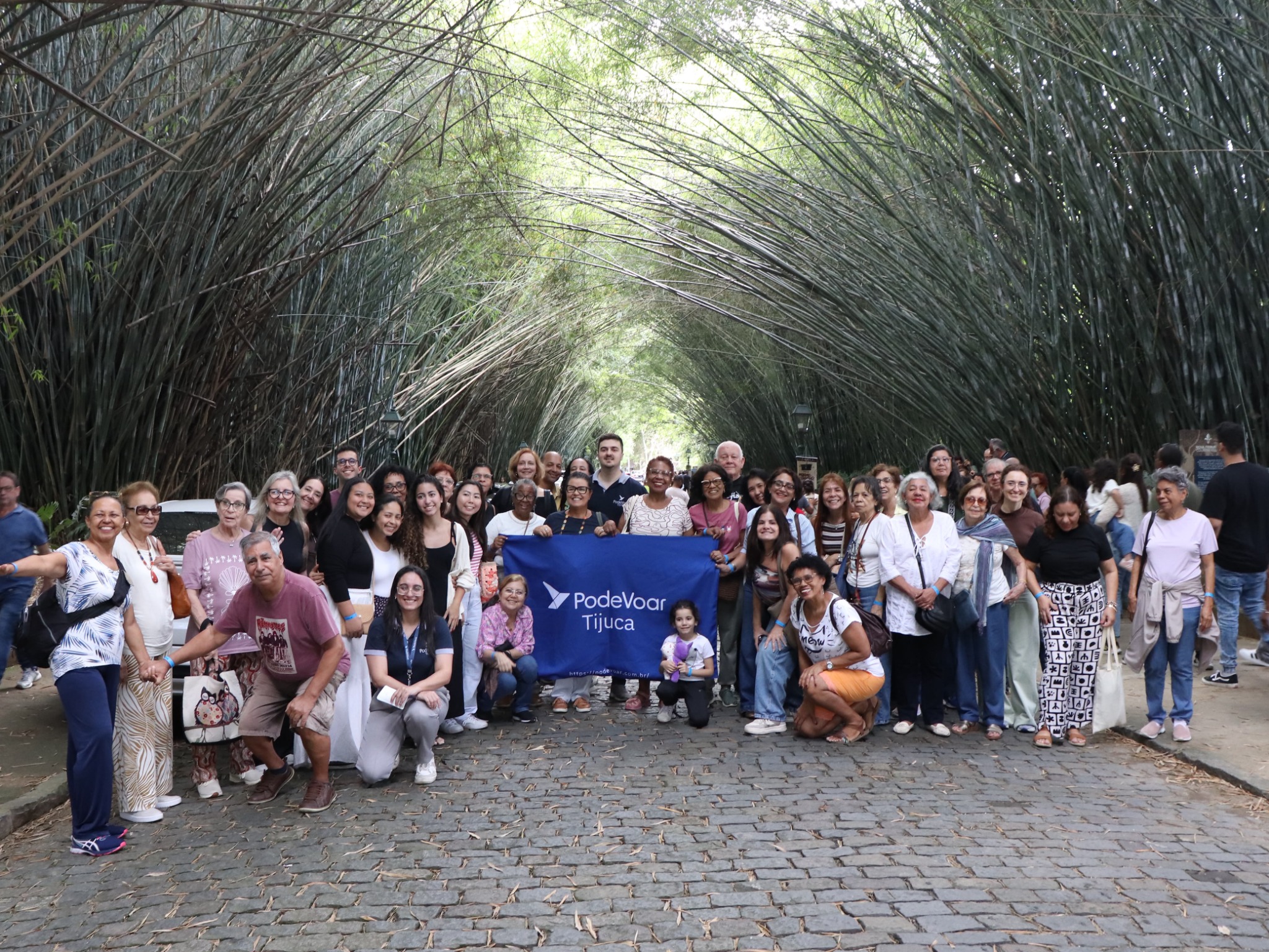 Grupo da excursão da PodeVoar Tijuca em Nova Friburgo, reunido sob um túnel de bambus com a bandeira da agência
